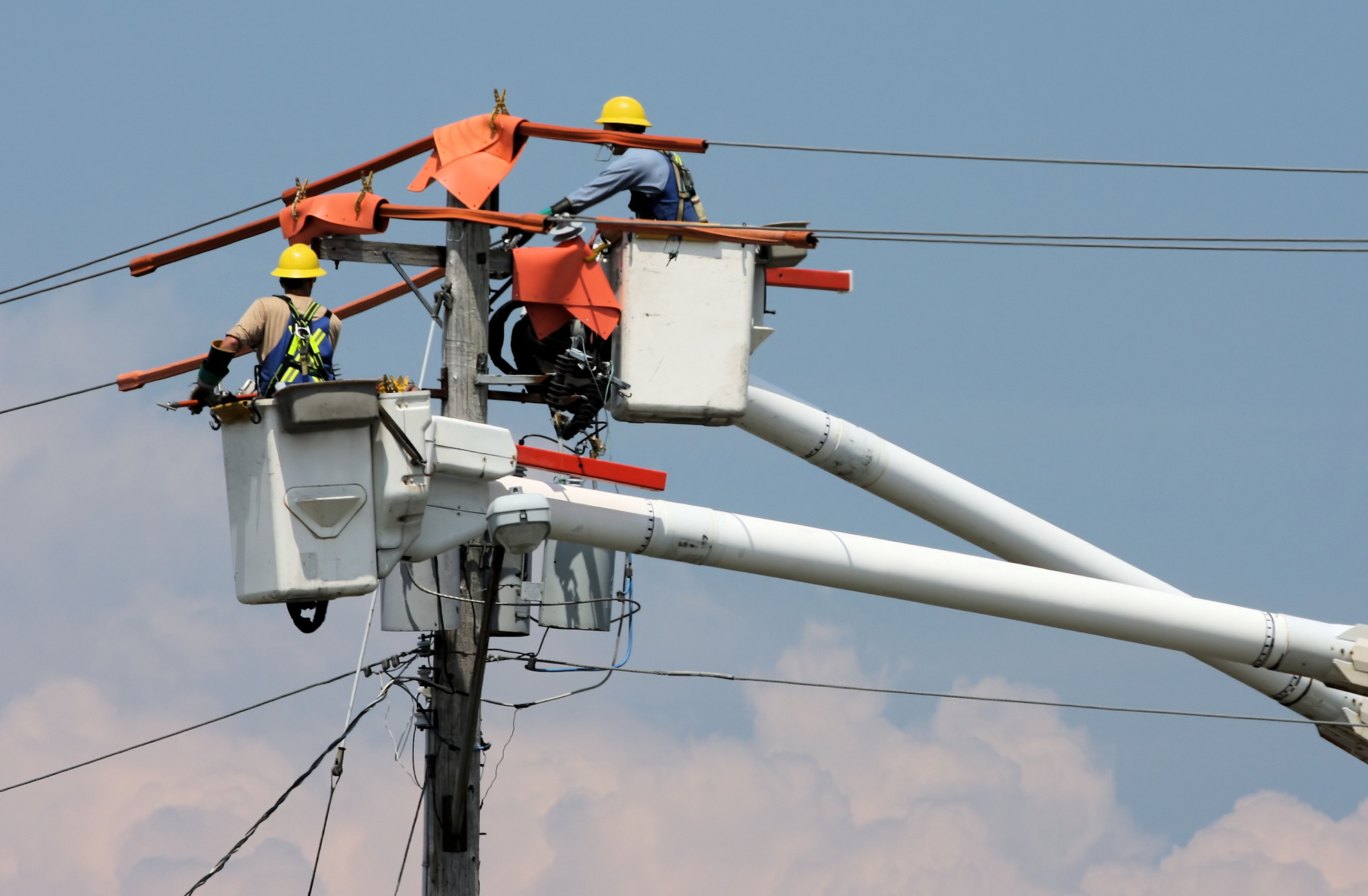 View of two electrical lineworkers working on electrical poles and wires in a bucket truck