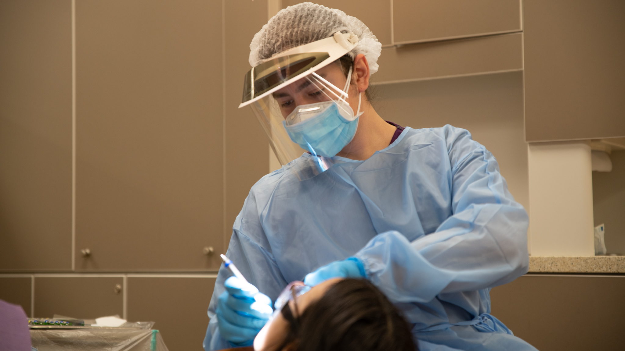 A dental hygenist conducts a procedure on a sitting patient.
