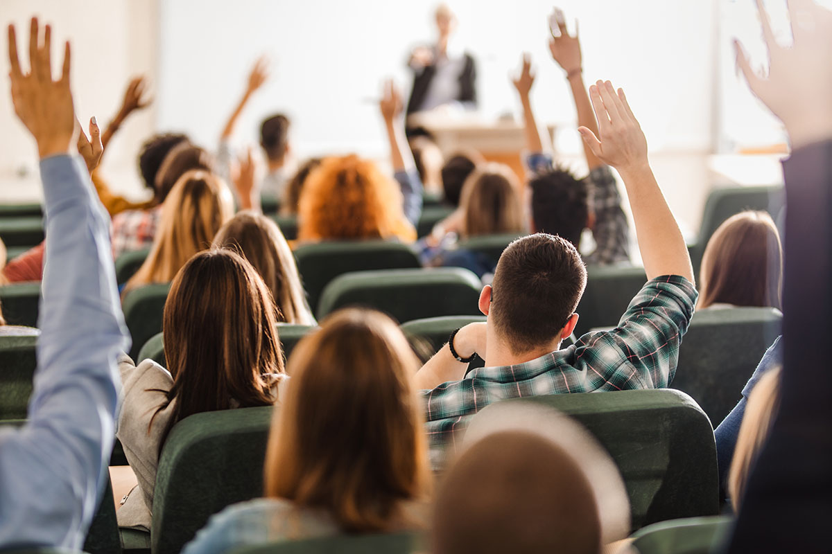 Group of students raising their hands from their seats in a classroom