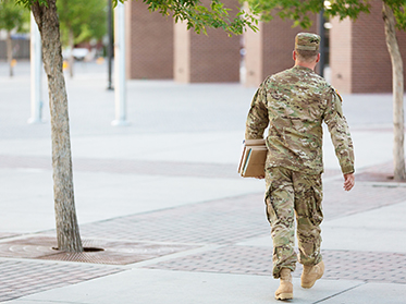 Student in Army fatigues carrying books across campus