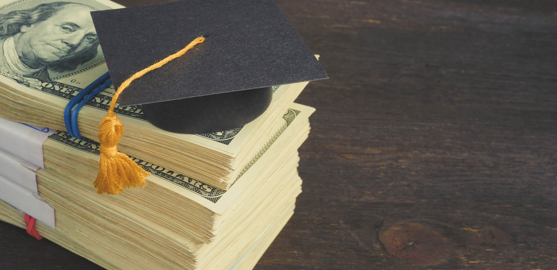 Graduation cap on top of a stack of $100 dollar bills