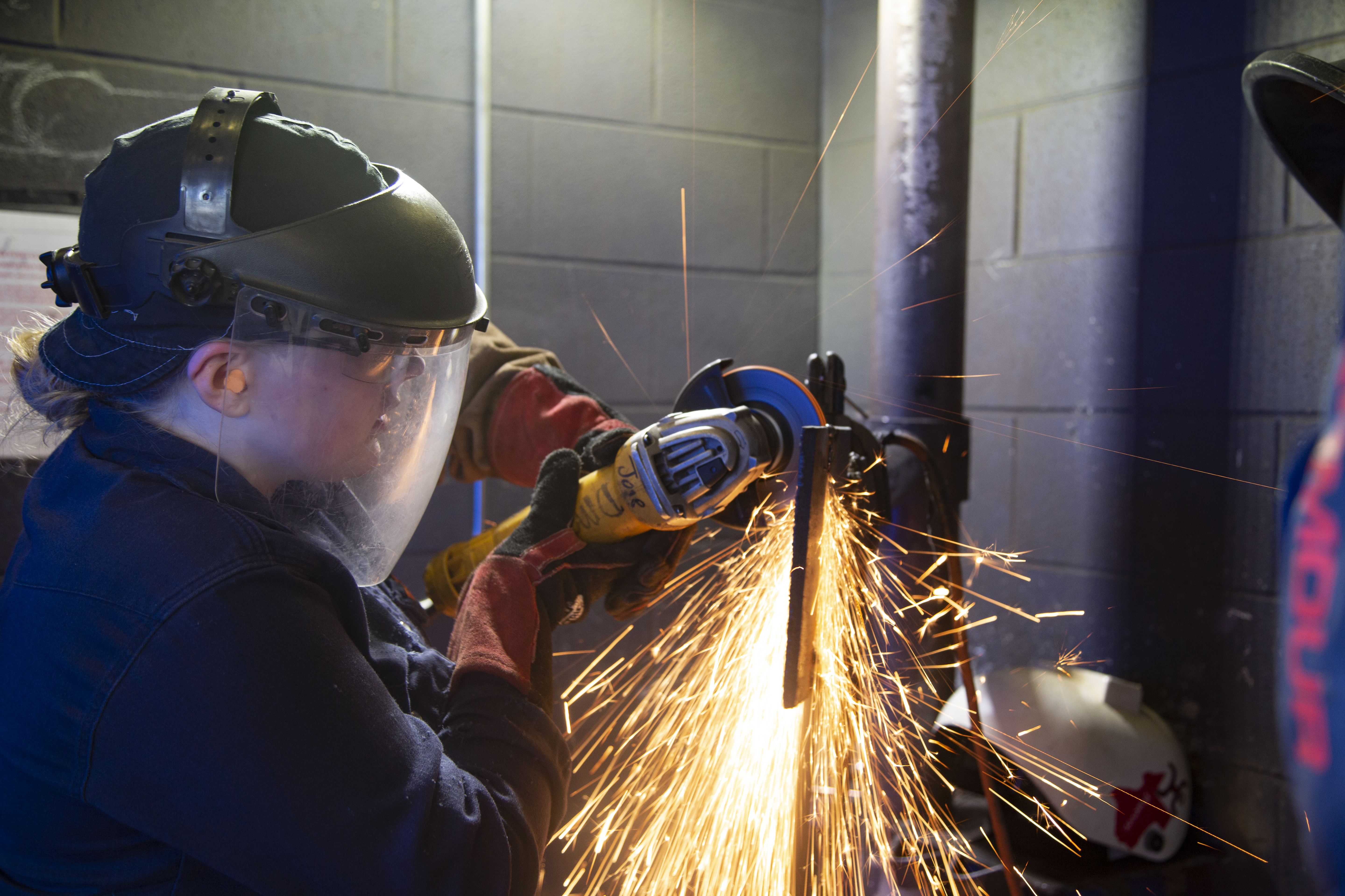 Sparks fly as a student wearing safety gear welds pipe