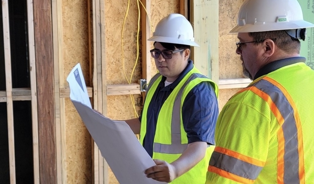 Two workers review blueprints at a construction site.