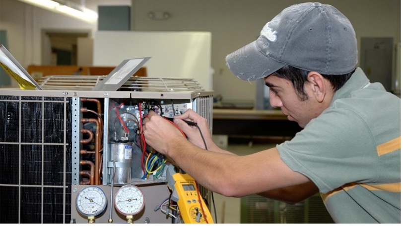 Man wearing a hat and working on an air conditioning appliance.