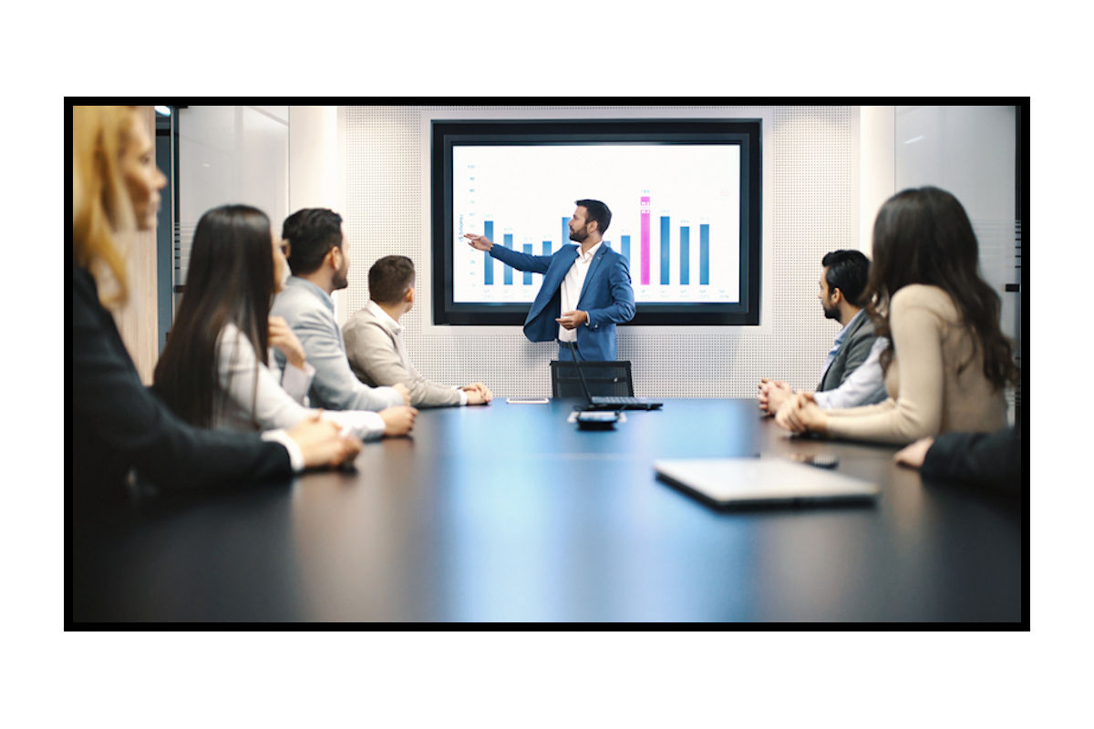 Man discusses financial graphs on screen to meeting of co-workers