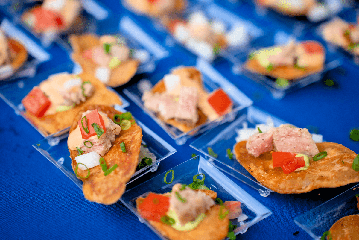 Gourmet appetizers on chips with tuna, tomato, and green onions on trays.