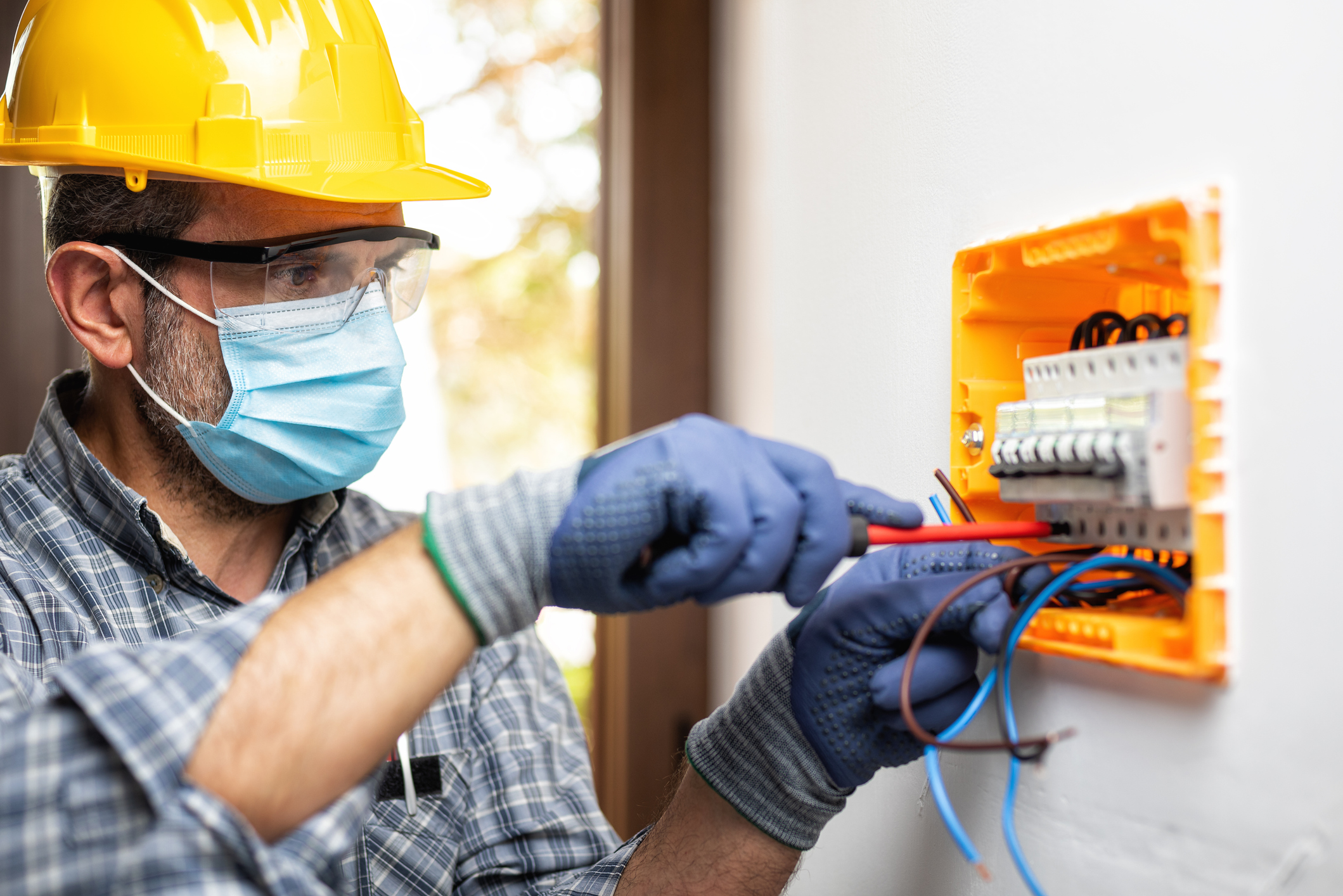 Electrician in a hard hat and medical face mask.