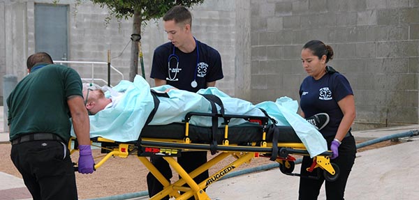 Two EMT students are putting a fake dummy doll on a stretcher and practicing regular procedures.