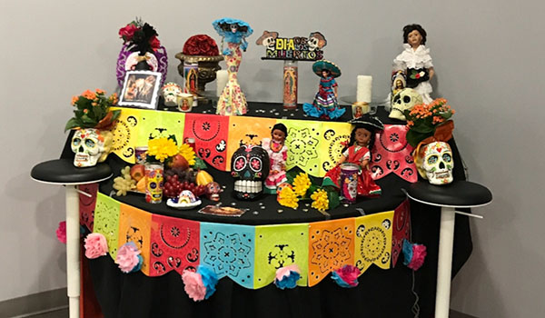 Flowers, calaveras, dolls and candles are displayed on a Día de los Muertos altar