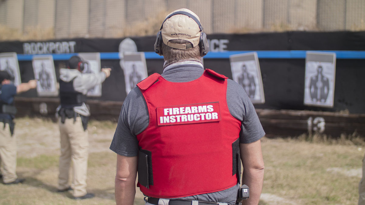 Main wearing firearms instructor vest watches as trainees practice shooting targets