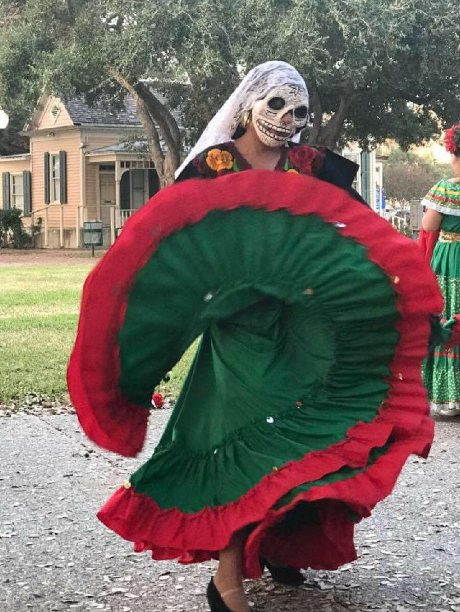 Teresa Saldivar dancing in her folklorico dress and a skull mask.