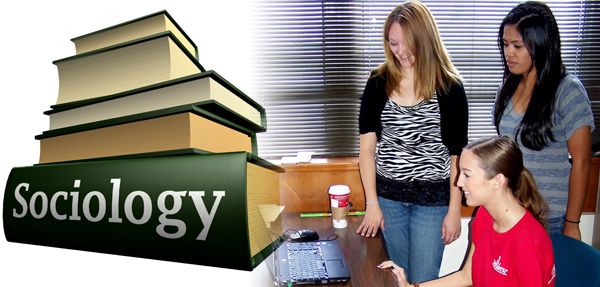 A book about sociology sits on a table next to students looking at a laptop.