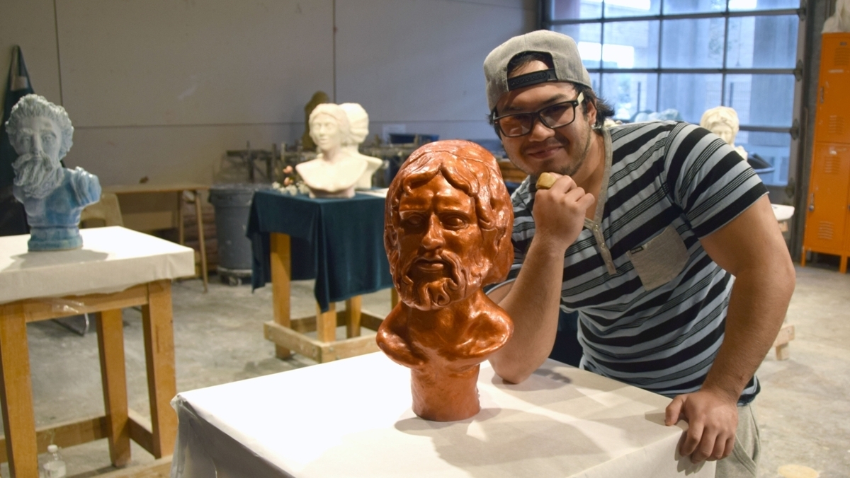 Student smiles while standing next to a sculpture of a bearded man