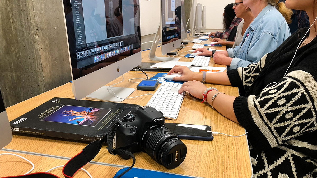 Students edit photos at a row of computers in the digital photo lab