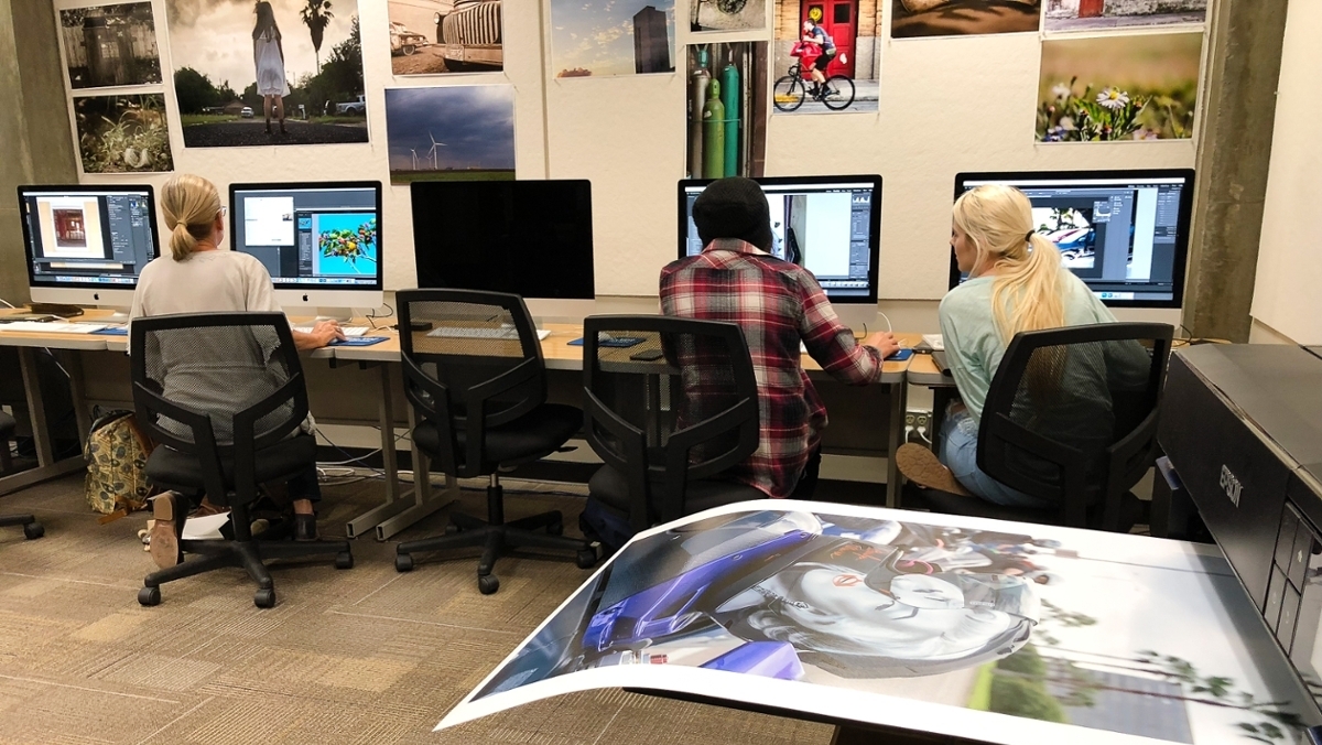 A digital photo is printed in the foreground while students work on iMacs