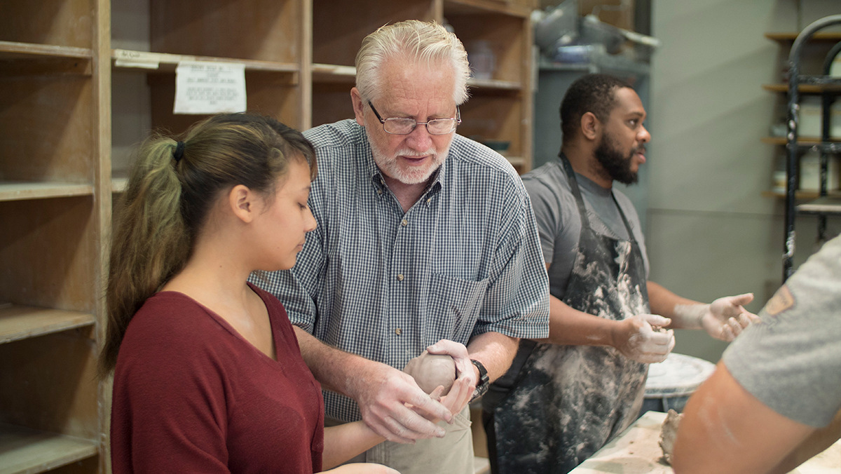 An instructor helps a student with clay