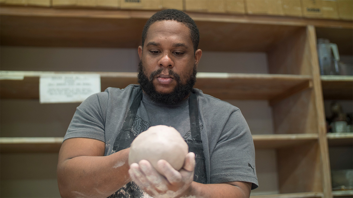 A man works a ball of clay in his hands