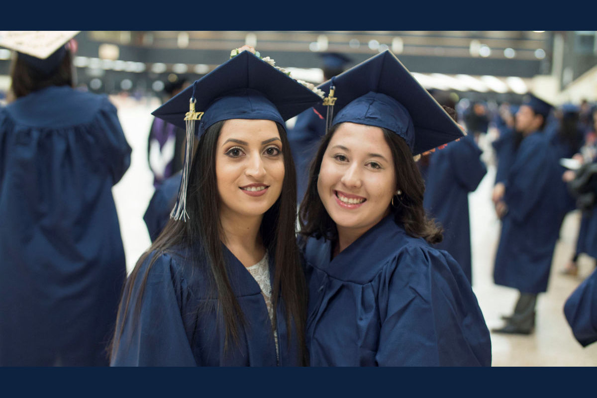 Students Sarai Morua and Sabrina Coleman smile and pose together in their graduation caps and gowns