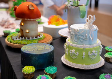 Collection of decorative cakes, including a tiered green cake, a galaxy-themed cake, and a mushroom house cake.