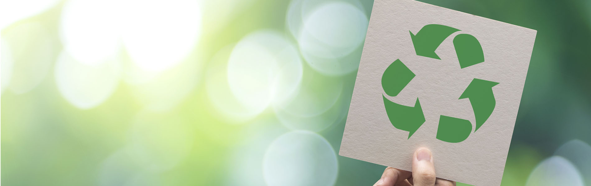 A hand holding up a cardboard sign with the recycling symbol
