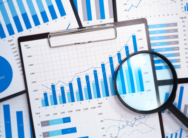 Several financial reports on a desk with a magnifying glass on top