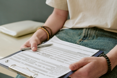 Person holding a clipboard with an unreadable printed form while seated in jeans.