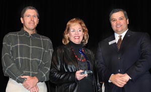 Exie Hall accepts an award onstage from Brian Hart and President Mark Escamilla.