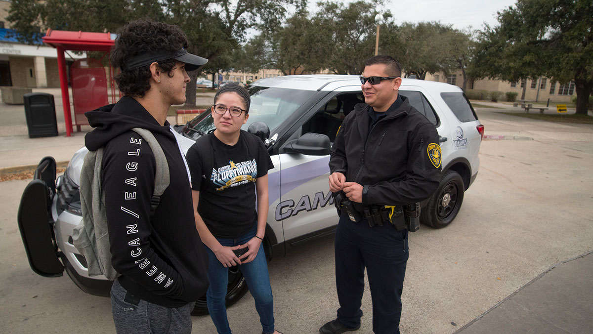 Campus Security officer talks with a male and female student next to a DMC security SUV.