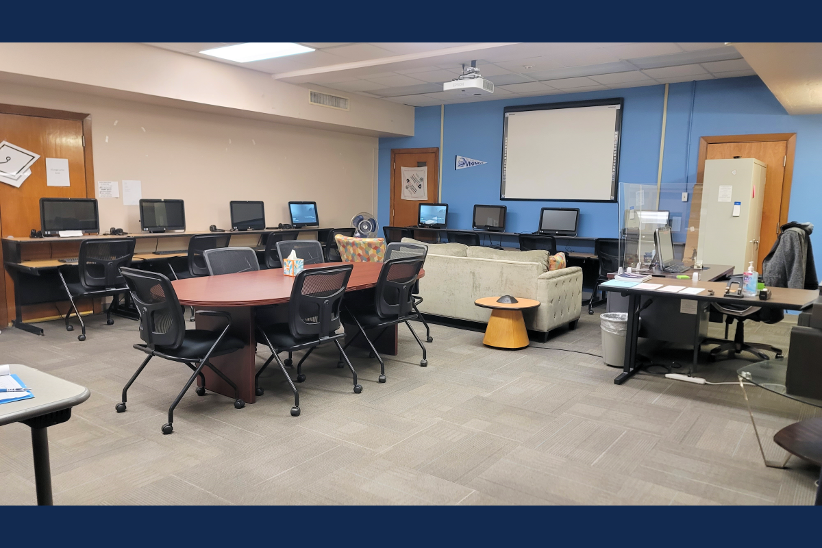 Heritage Campus Veteran's lounge with desks, chairs, computers, a sofa, and a projector screen.