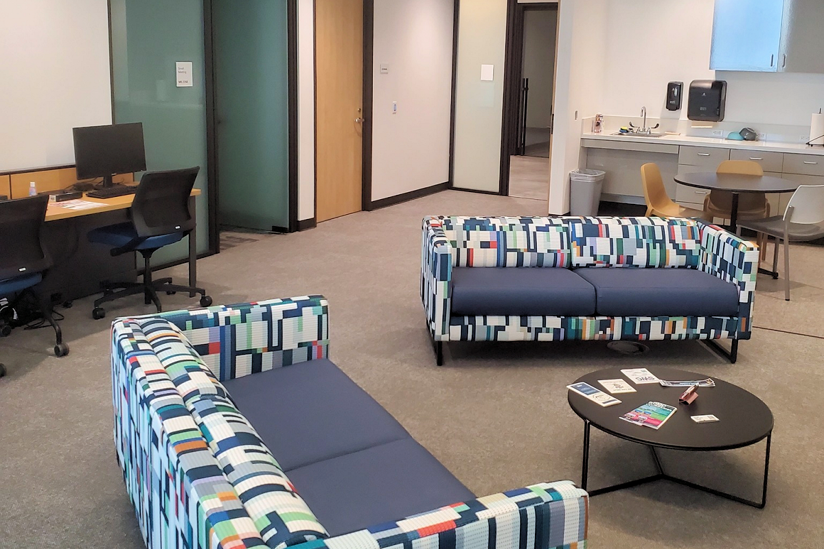 Oso Creek Campus Veteran's lounge area with patterned sofas, a coffee table, and a desk with computer monitors.